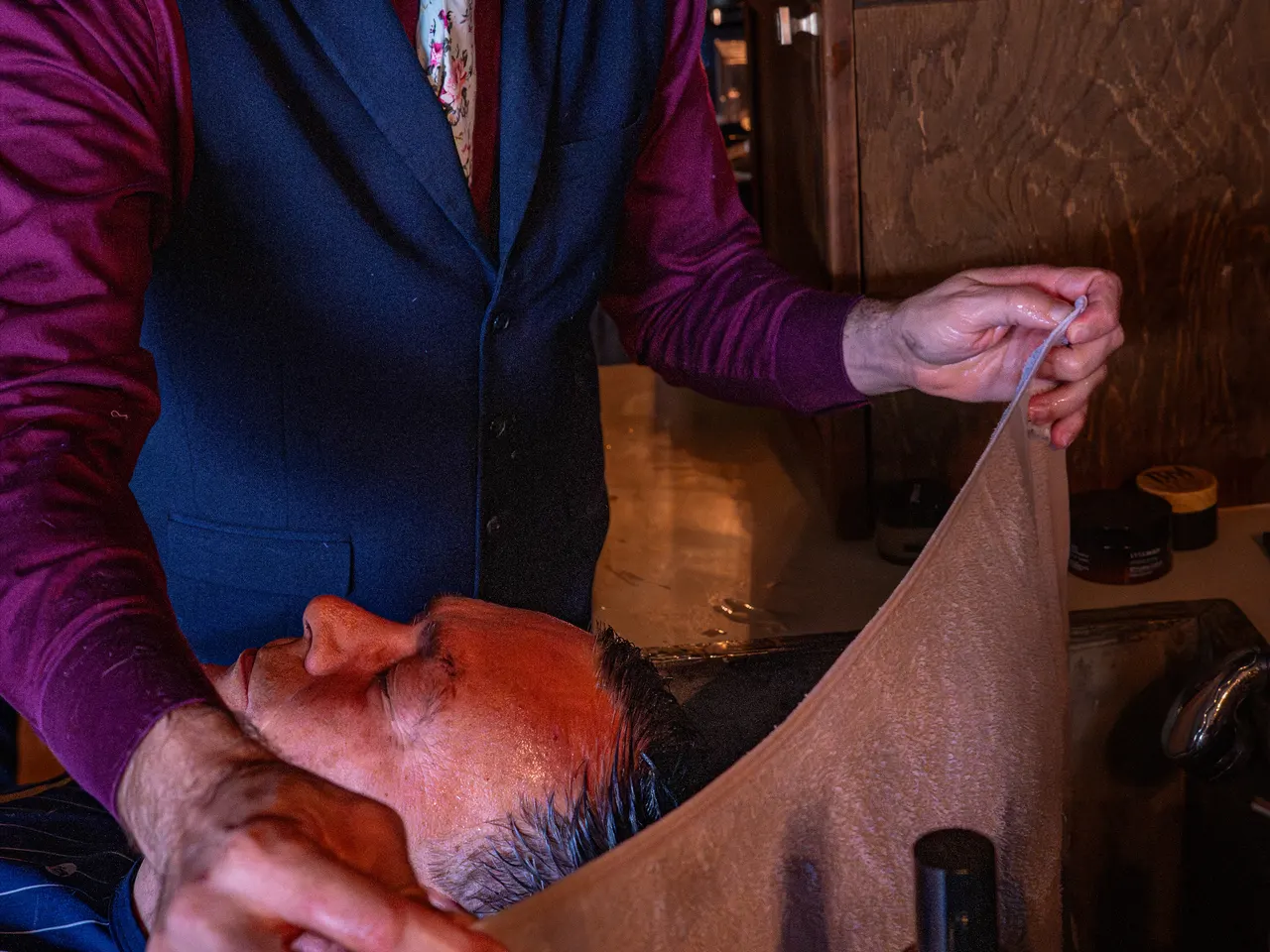 A barber laying a steamed towel over a reclined client at Barley and Mane