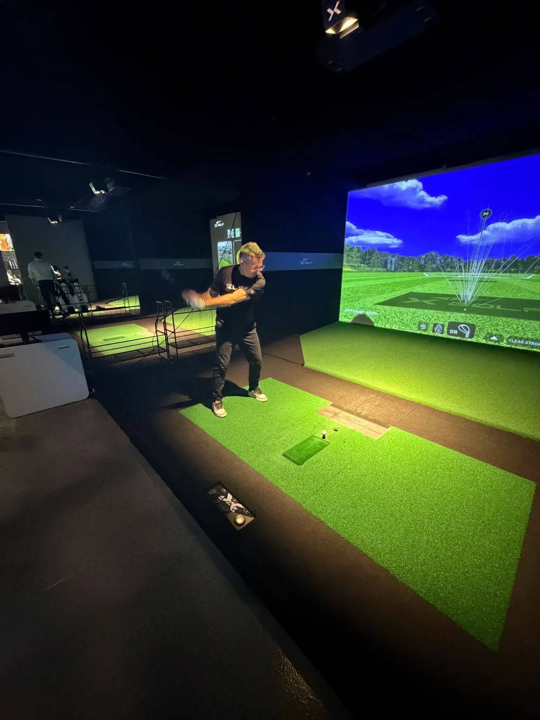 A member of the Barley and Mane team mid-swing at an indoor golf simulator