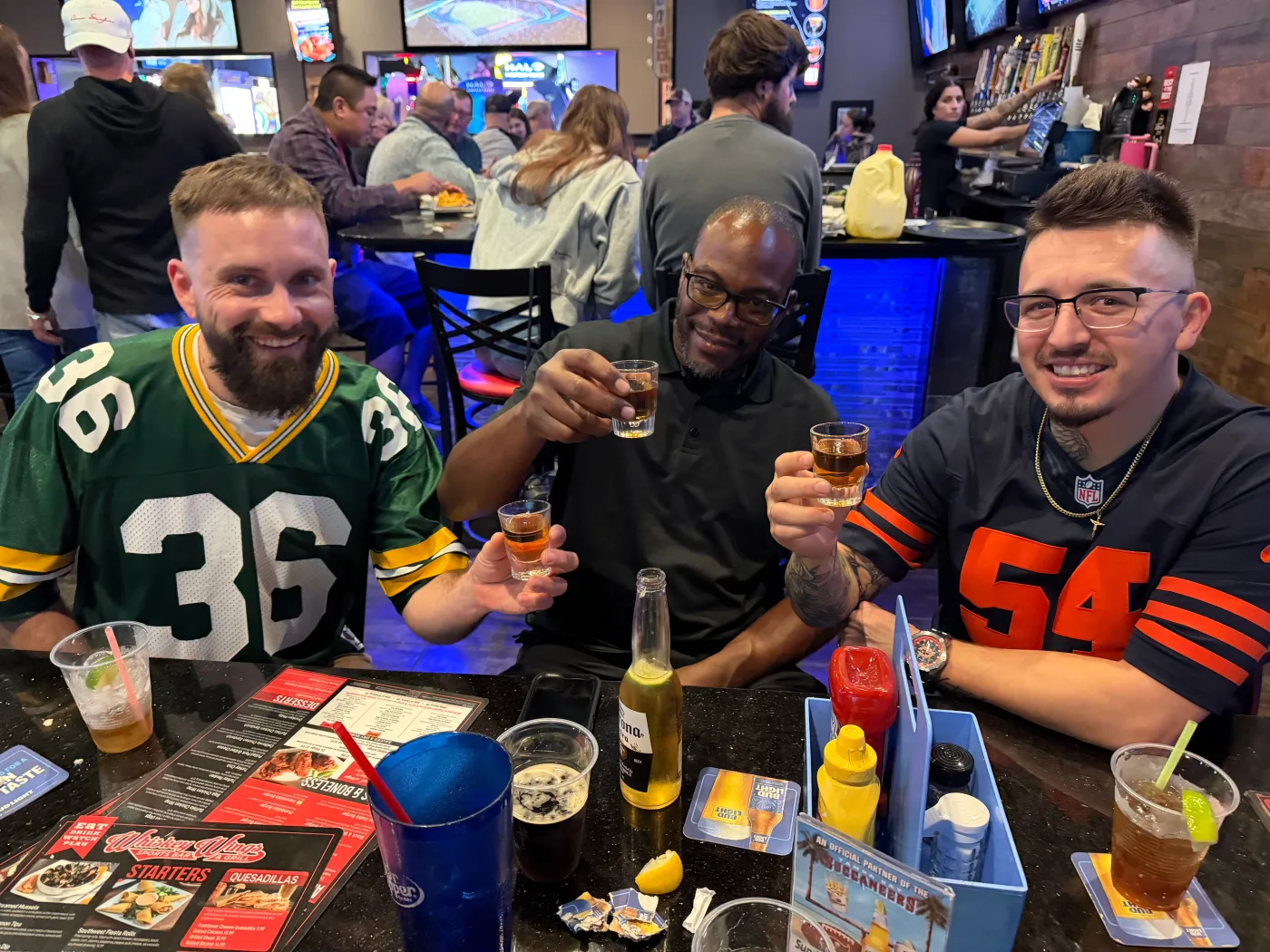 Three members of the Barley and Mane team raising a toast together at a sports bar