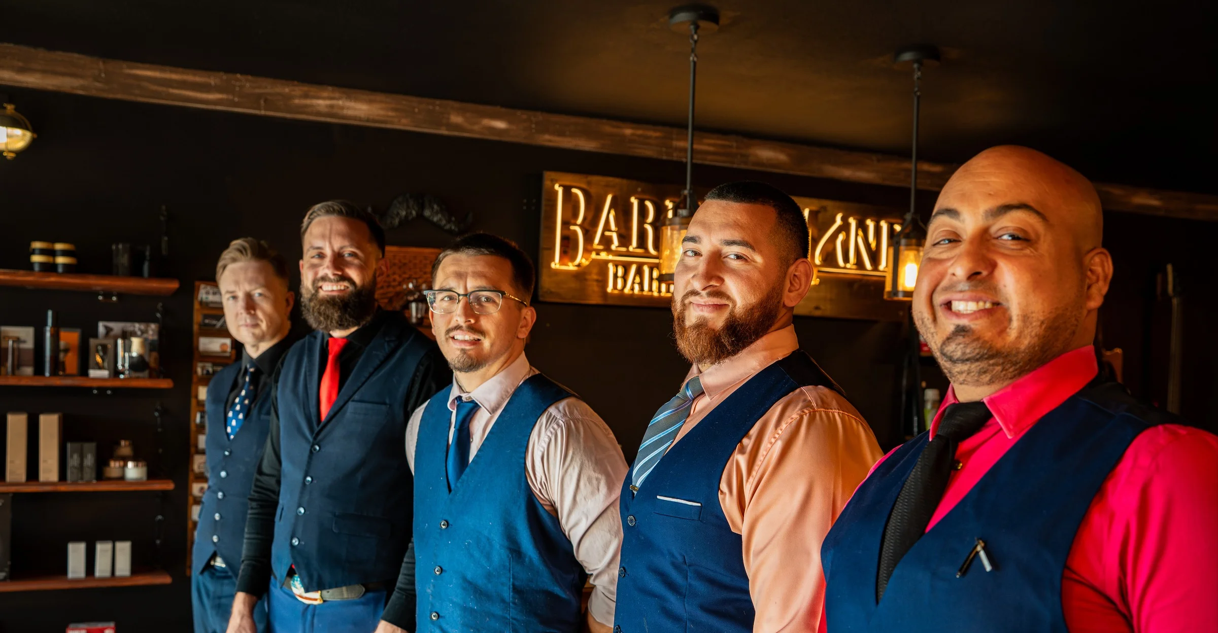 The Barley and Mane barbers in vests and ties lined up beneath the lit shop sign