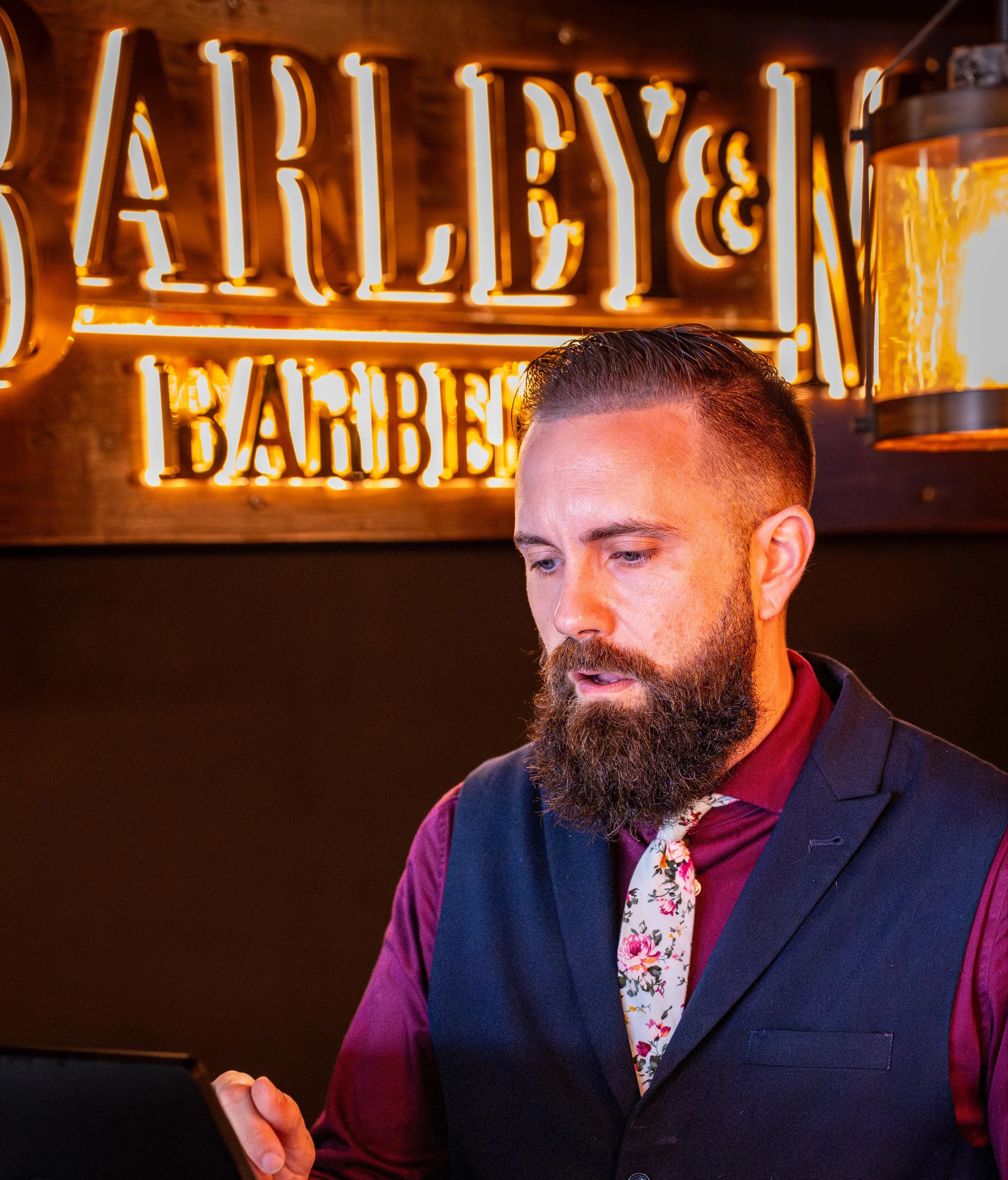 Owner Ryan beneath the lit Barley and Mane Barberspa sign inside the shop