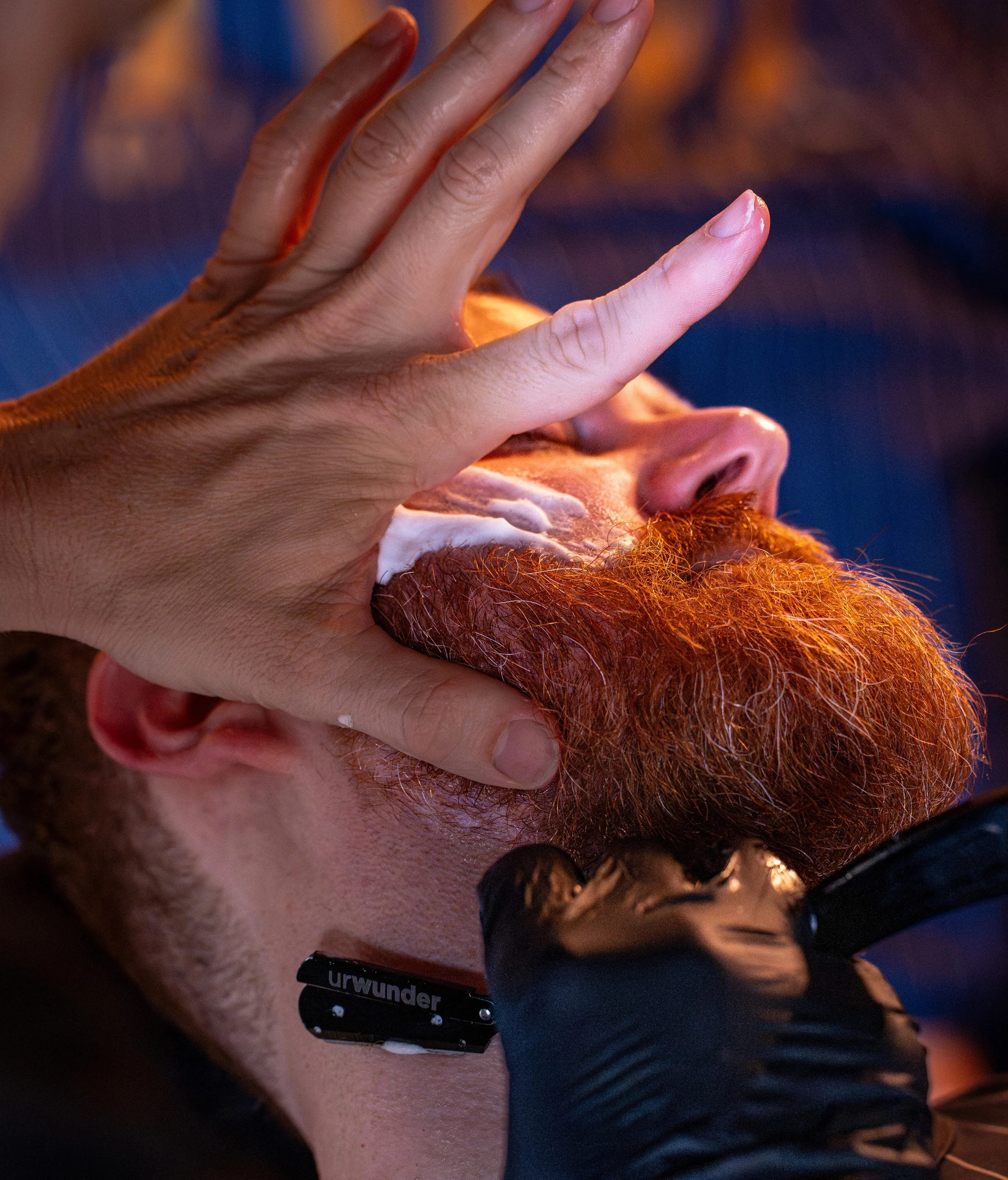 A barber steadying a client's head while working lather into a full red beard