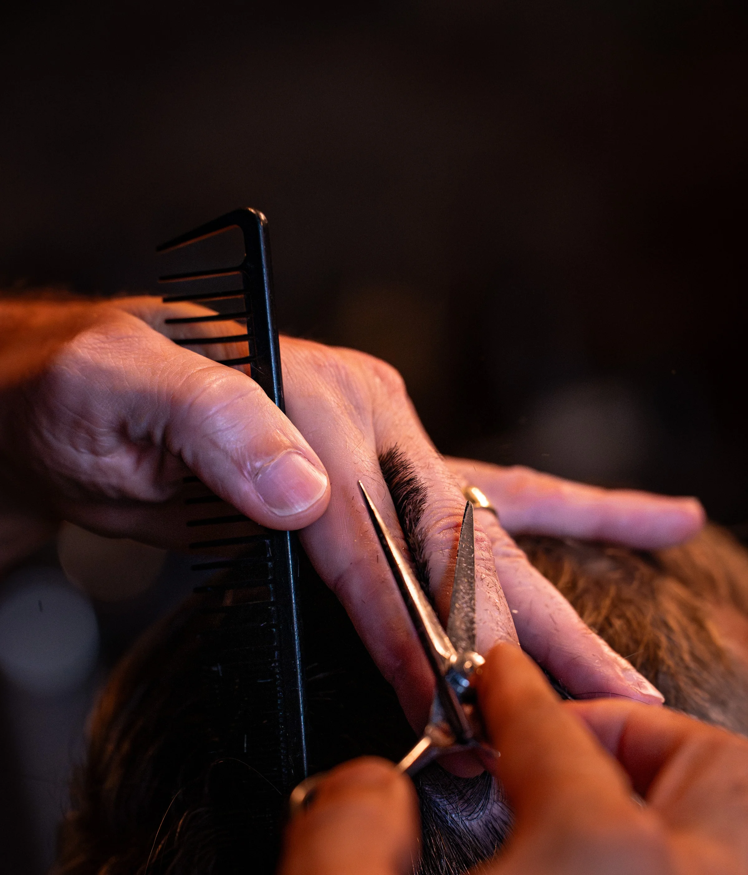 A barber's hands working a comb and blade through a client's hair, close up