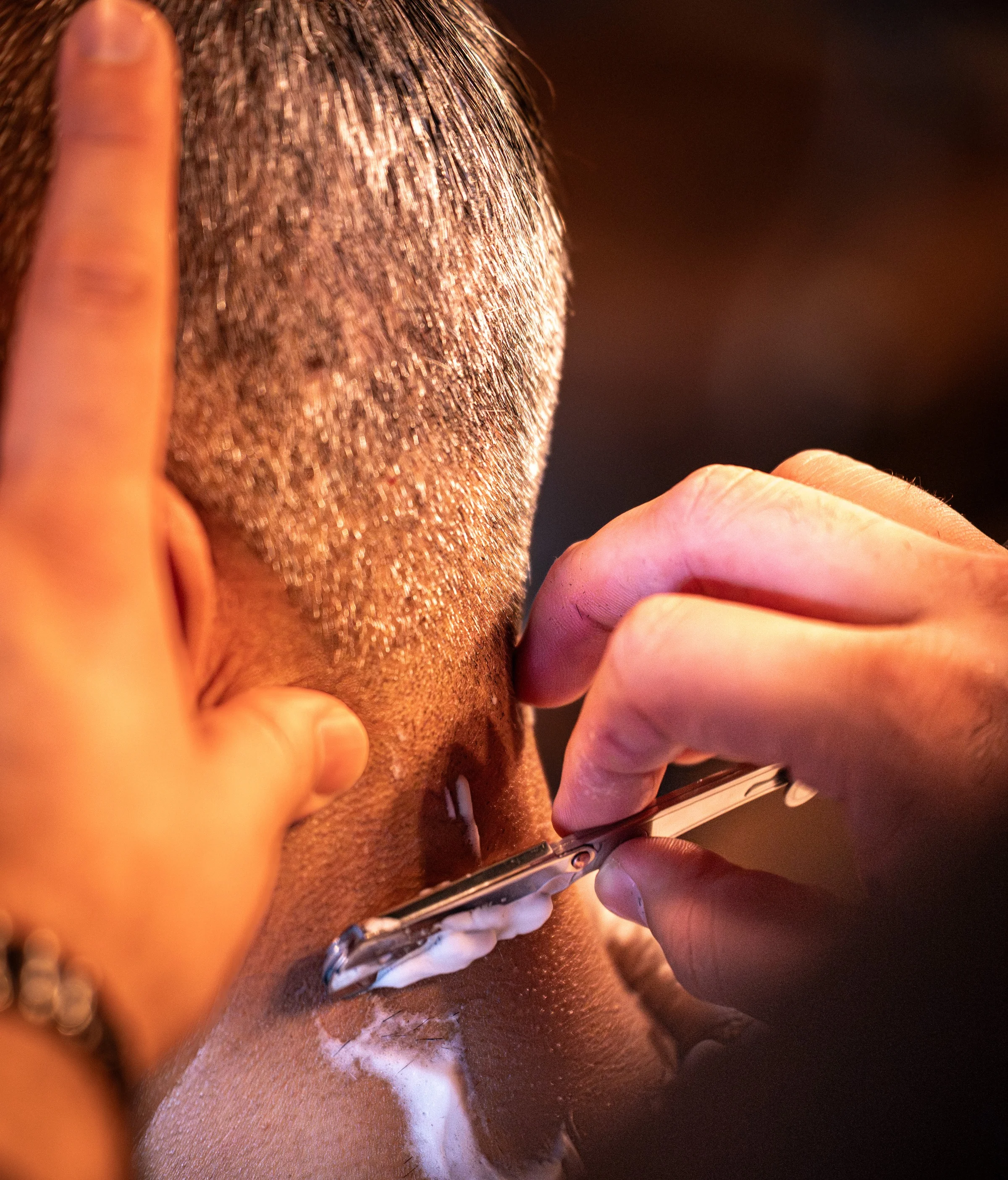 A barber finishing a client's neckline with a straight razor, close up