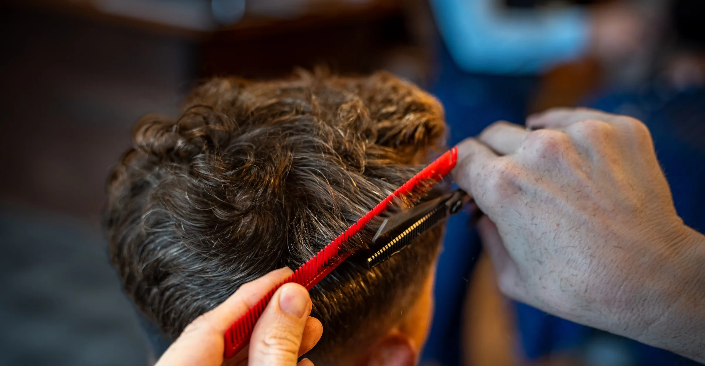 A Barley and Mane barber lifting a section of a client's hair with a red comb while cutting it close