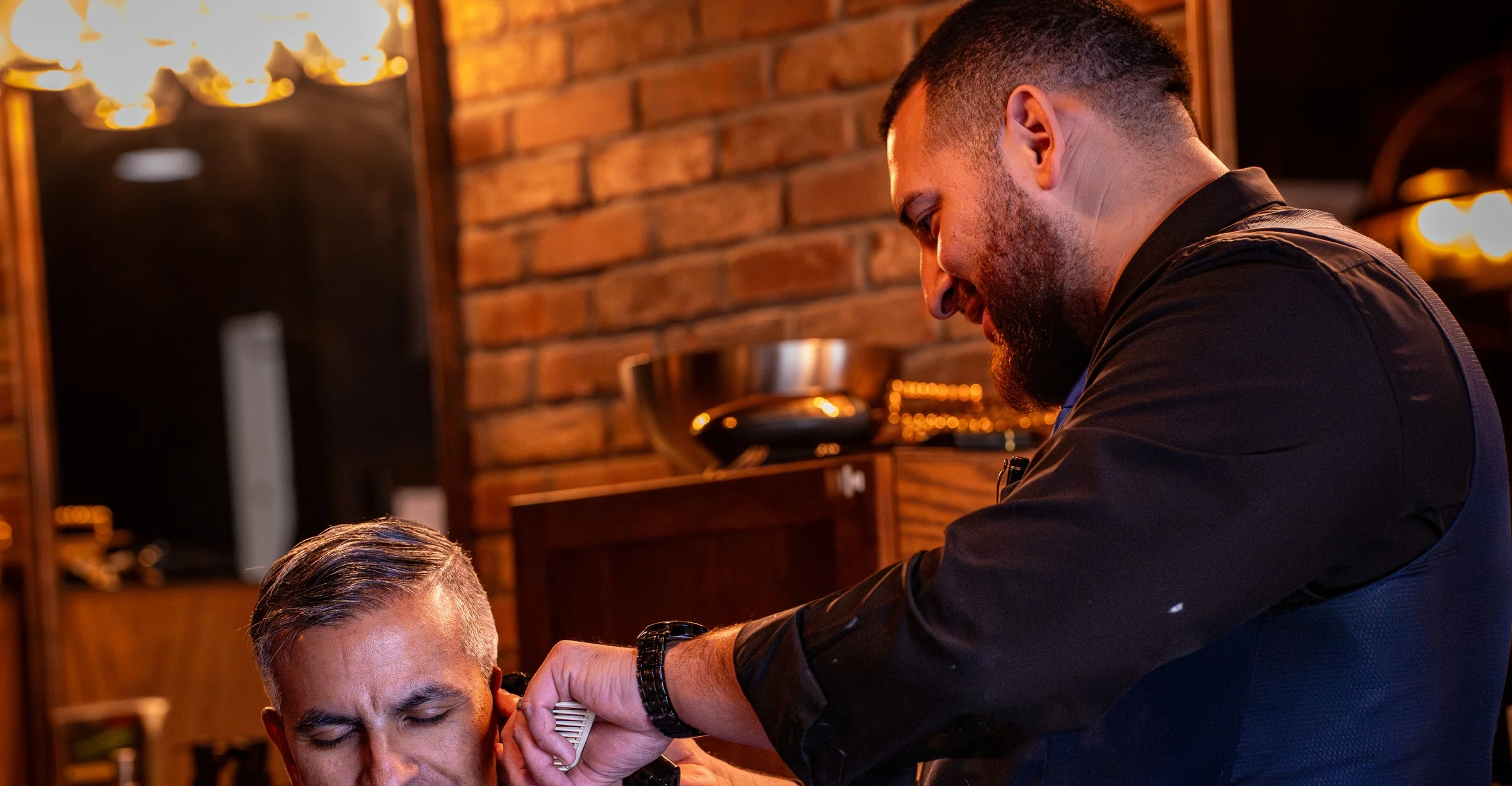 A smiling client in the chair while a Barley and Mane barber details the hair above his ear