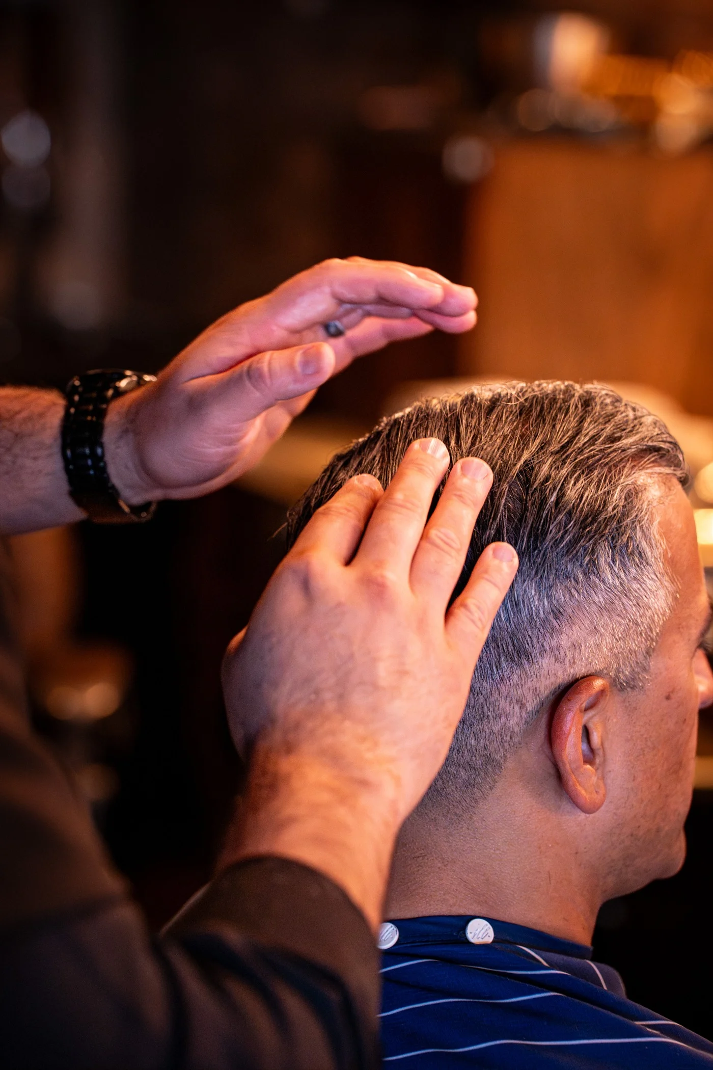 A barber's hands lifting and shaping a client's salt and pepper hair