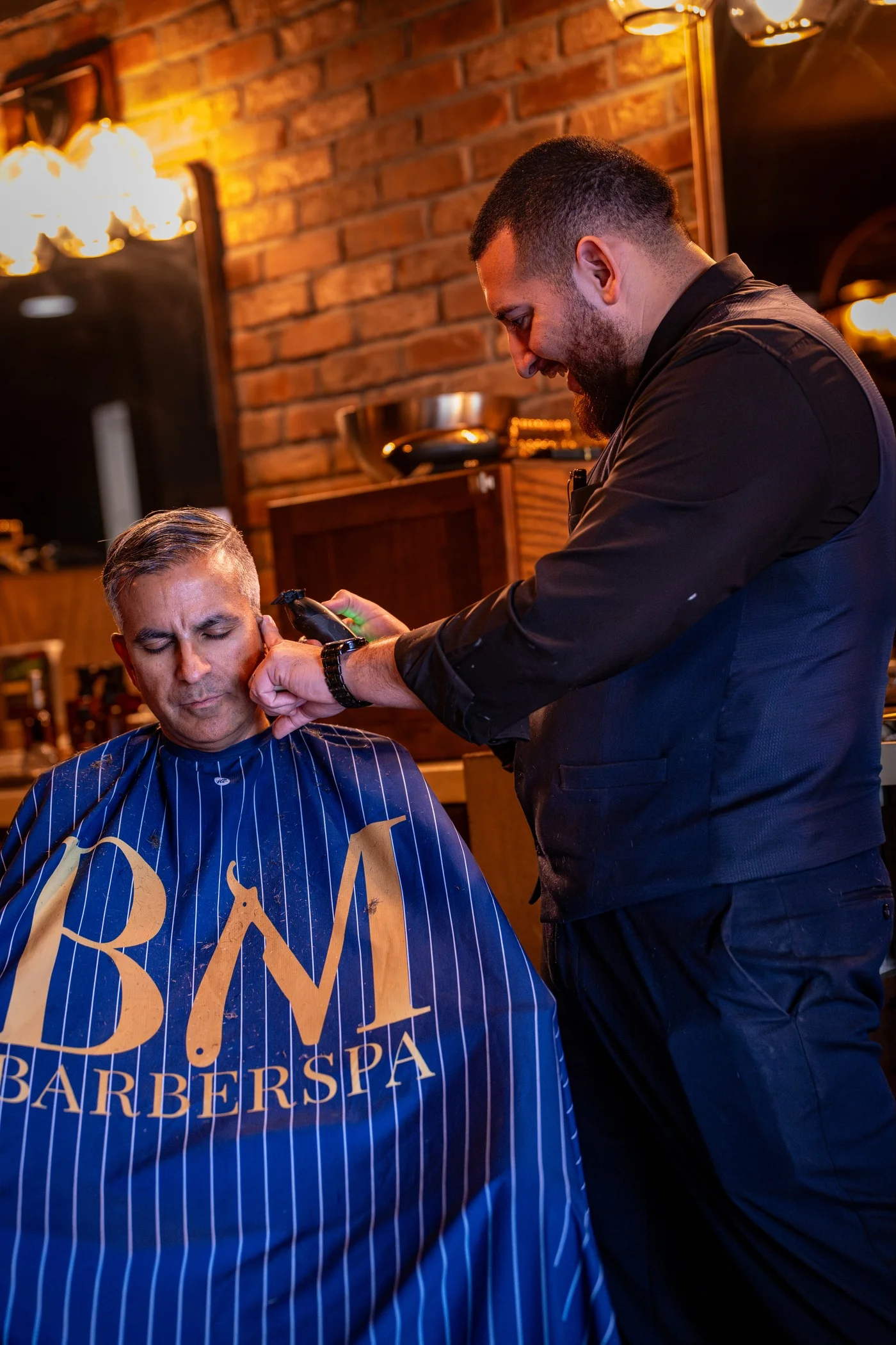A Barley and Mane barber trimming the sideburn of a gray haired client wrapped in a Barley and Mane cape