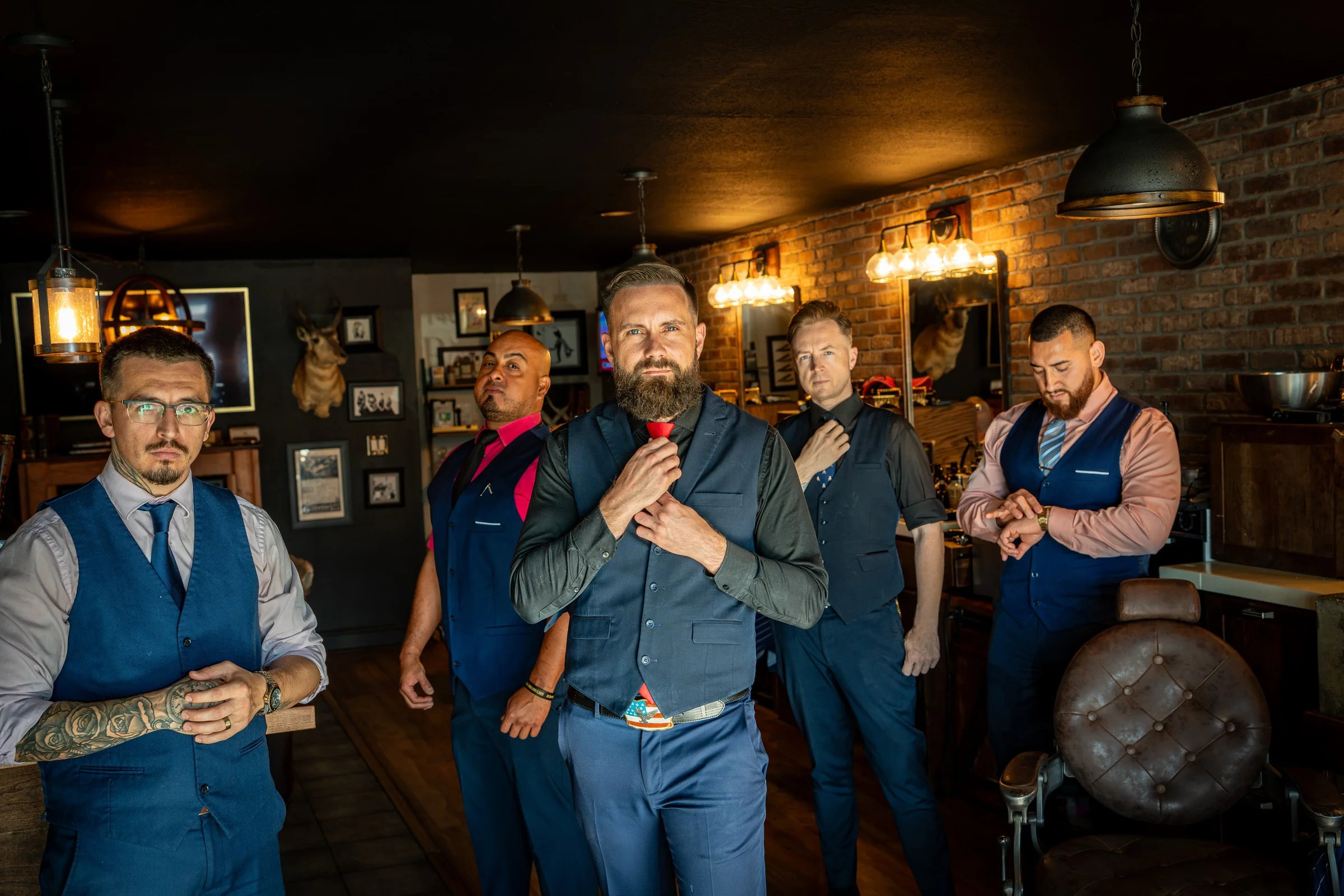 Five Barley and Mane barbers in vests straightening their ties together on the shop floor