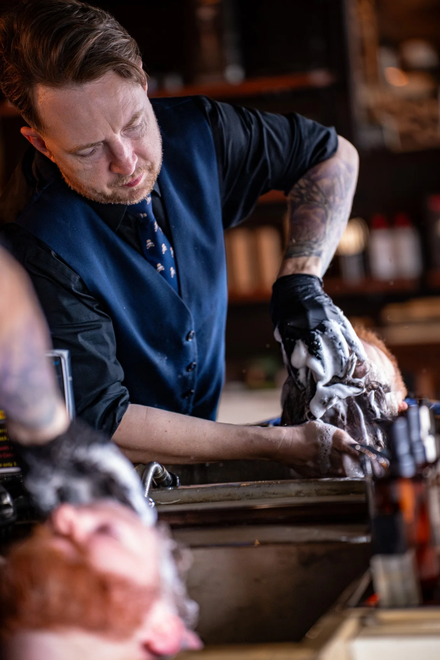 A Barley and Mane barber in black gloves shampooing a reclined client at the sink