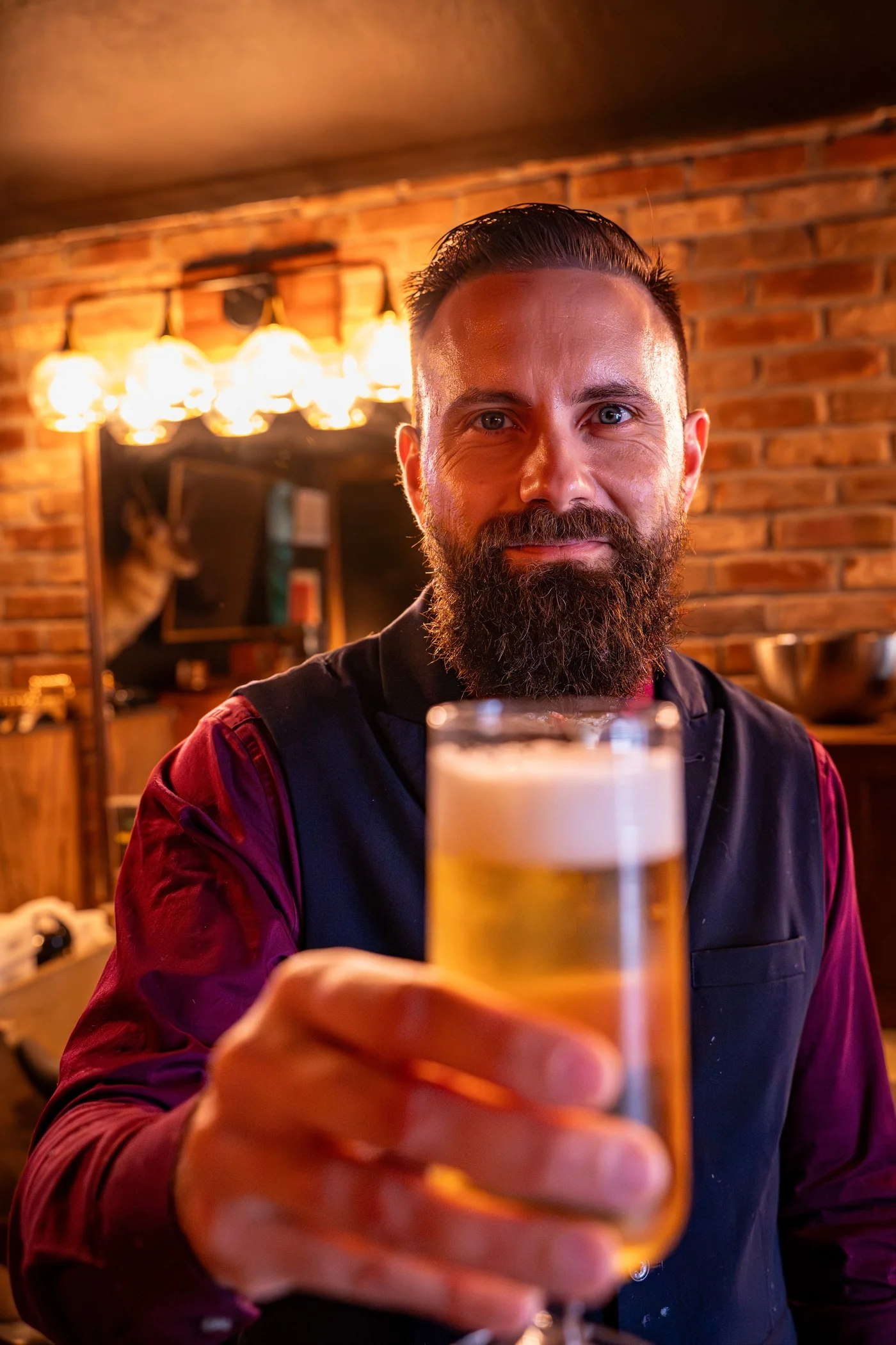A bearded Barley and Mane barber holding a freshly poured beer out toward the camera