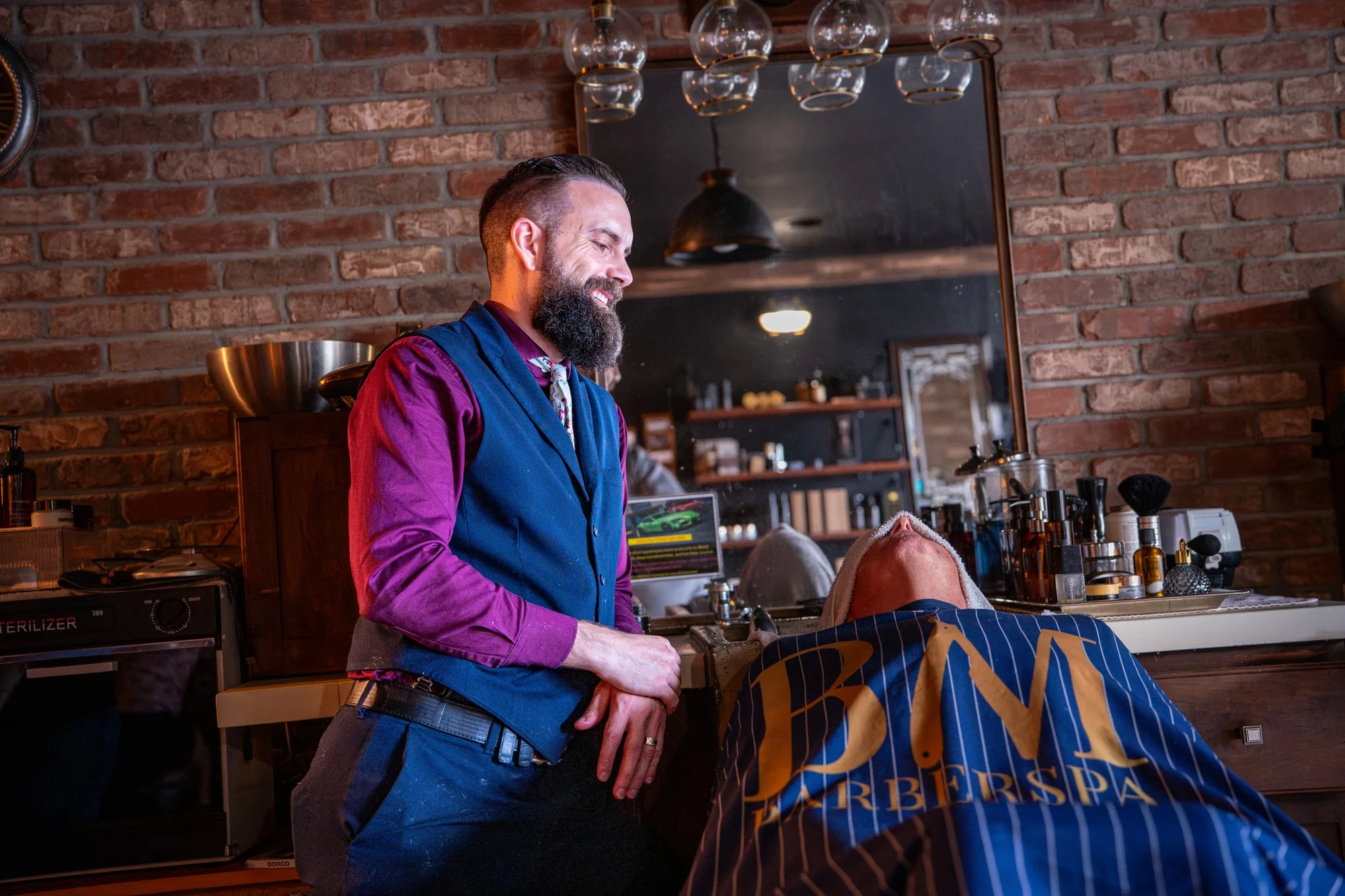 Owner Ryan leaning against the counter beside a client in a Barley and Mane cape