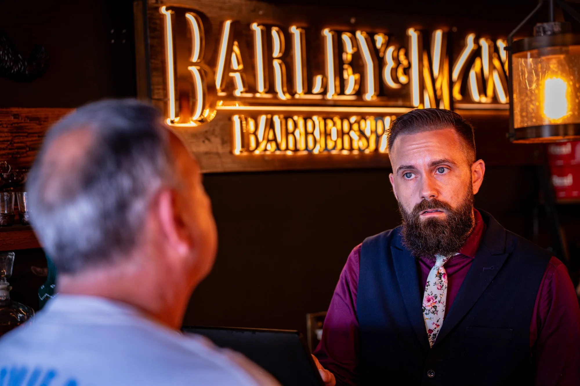 Owner Ryan talking with a client beneath the lit Barley and Mane Barberspa sign