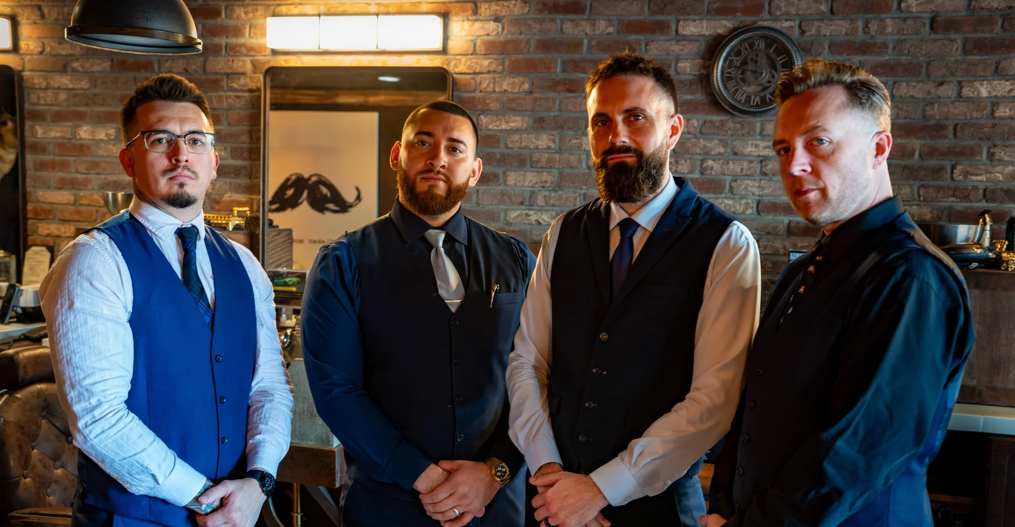 Four Barley and Mane barbers in vests and ties standing together inside the shop