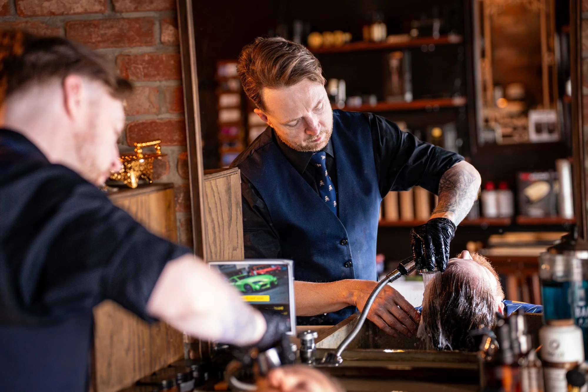 A Barley and Mane barber in gloves rinsing a client at the shampoo sink