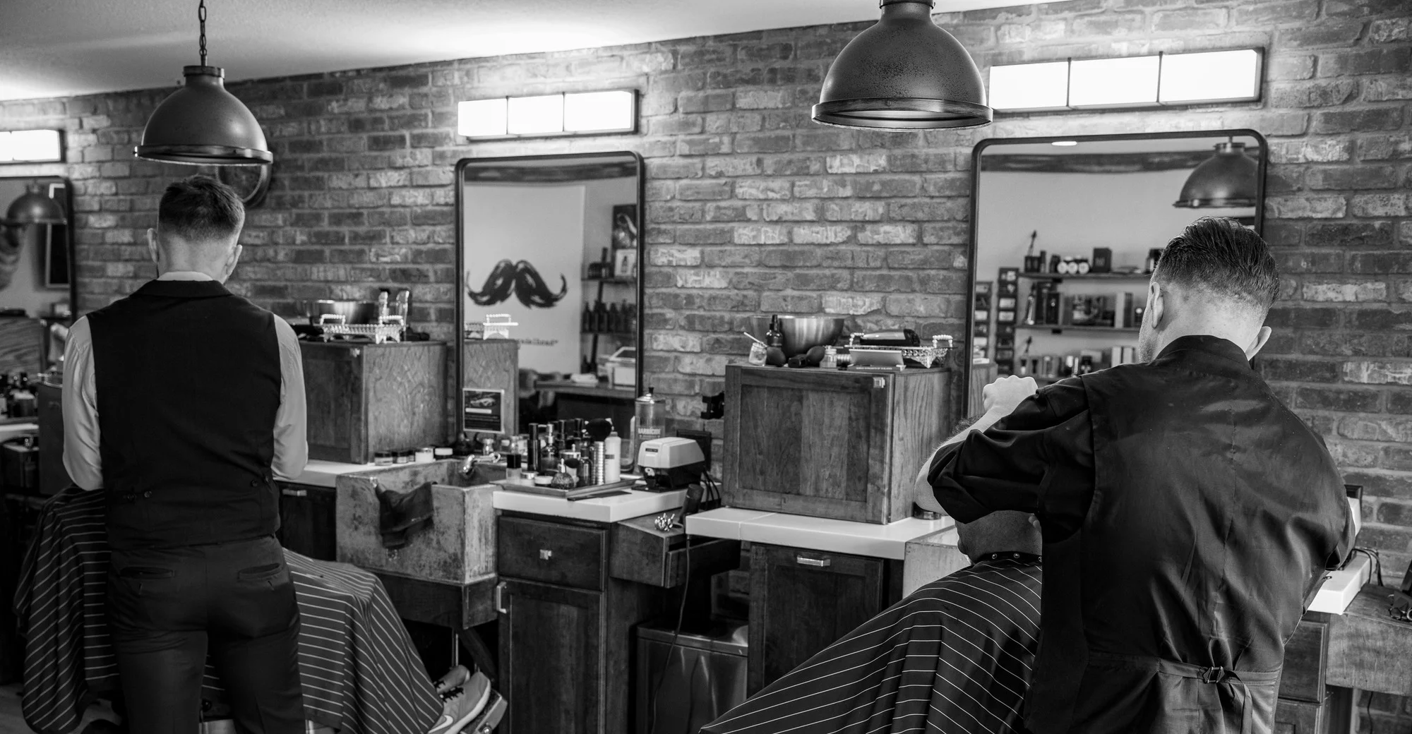 Two Barley and Mane barbers working side by side at their stations, in black and white