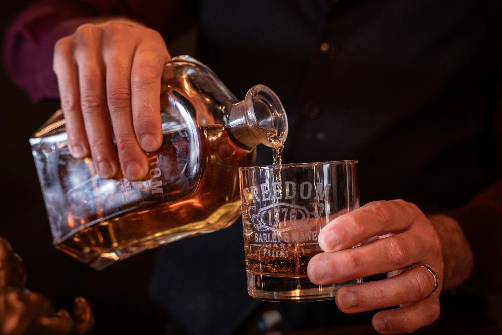 Whiskey poured from a crystal decanter into an etched Barley and Mane rocks glass